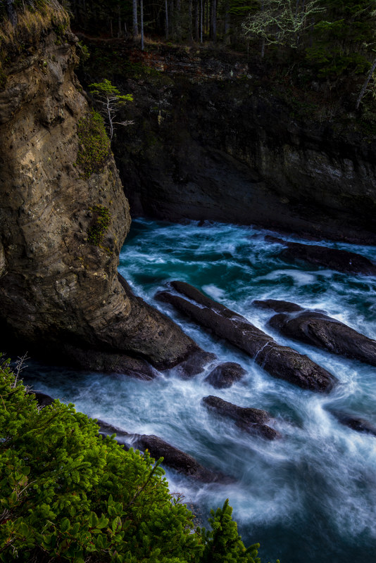 Wide view of the sea canyon at Cape Flattery with turquoise water churning below dark cliff walls